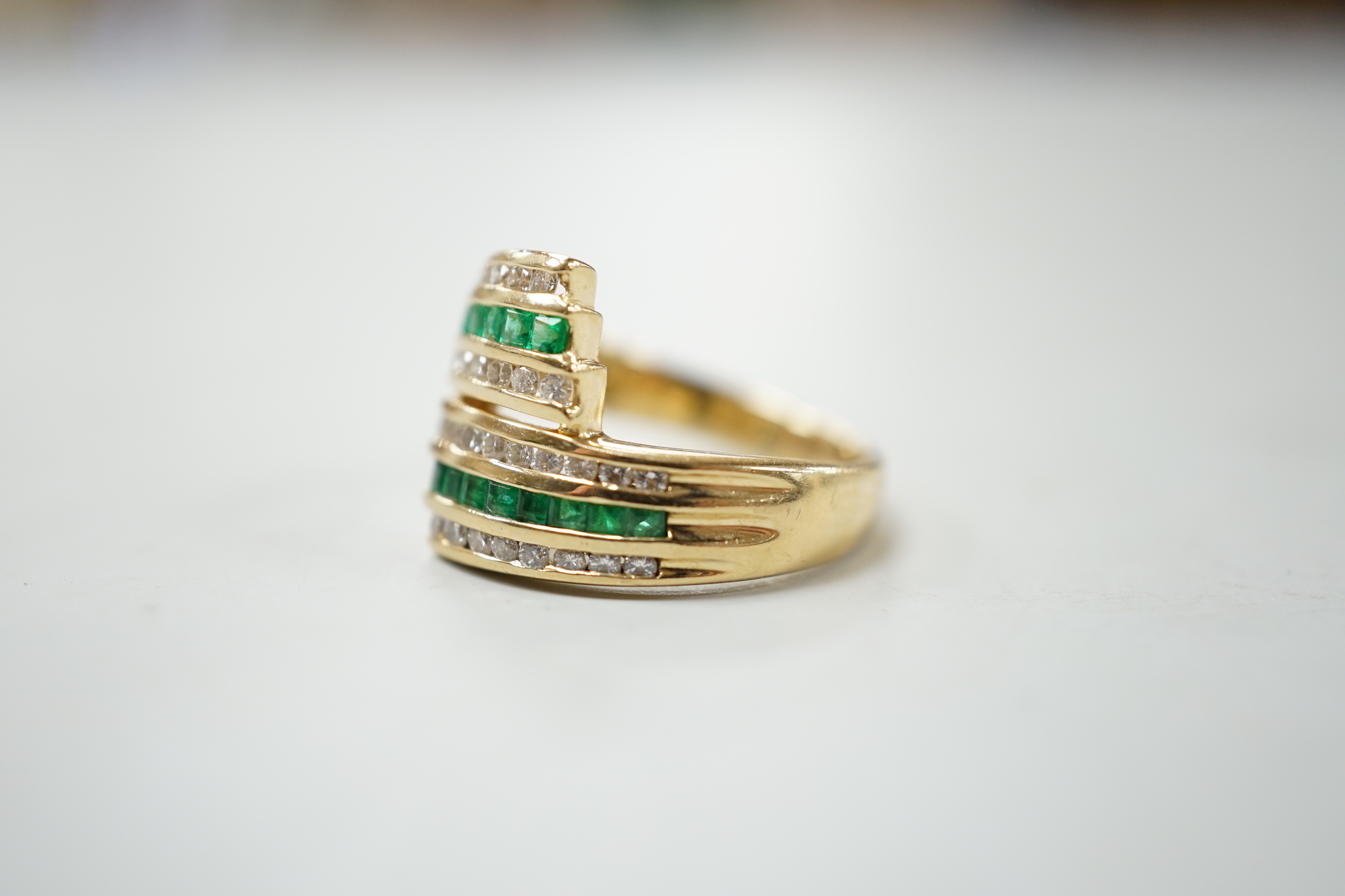 A modern 14k yellow metal, emerald and diamond chip set triple row crossover ring, size O, gross weight 5.4 grams.